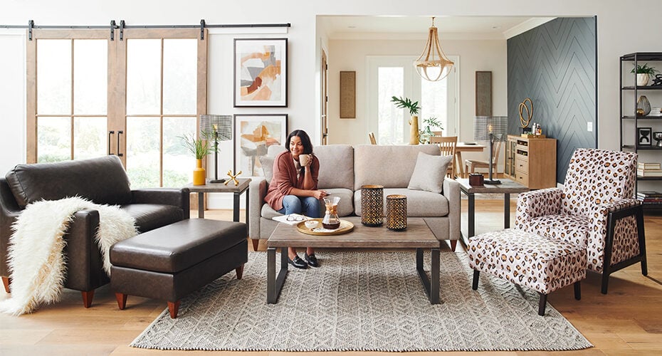 Lady enjoying coffee on beige loveseat with brown leather accent chair and cheetah accent chair